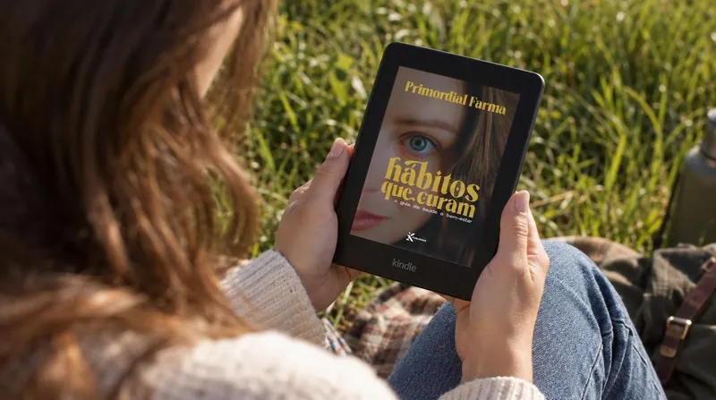 Mulher lendo Hábitos que Curam em um Kindle, sentada na grama ao sol